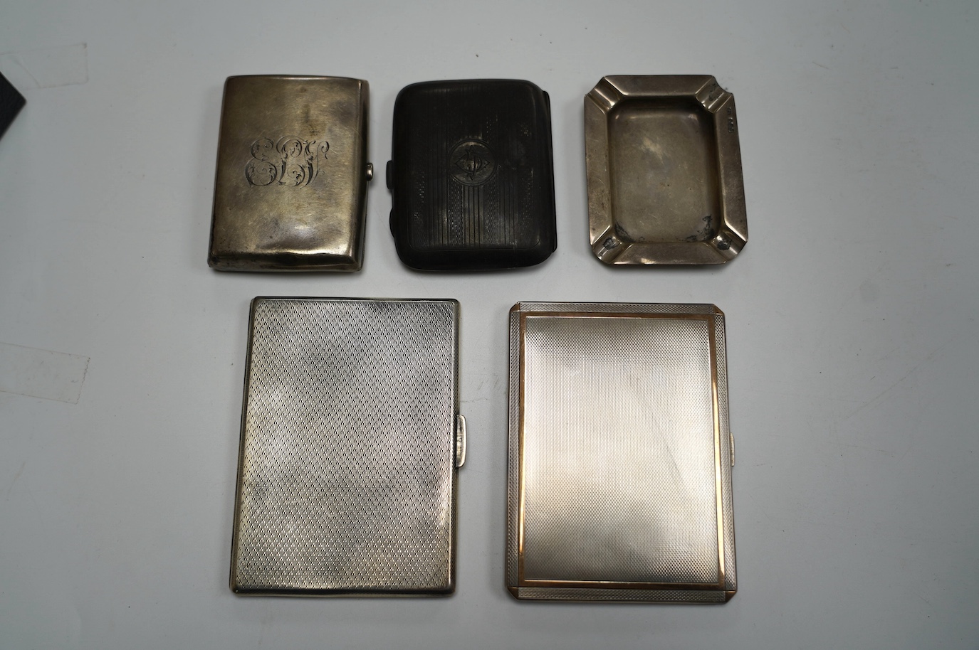 A George VI engine turned silver cigarette case, with yellow metal band, London, 1938, 11.4cm, four other silver cigarette cases and a silver ashtray, gross weight 16.8oz. Condition - poor to fair